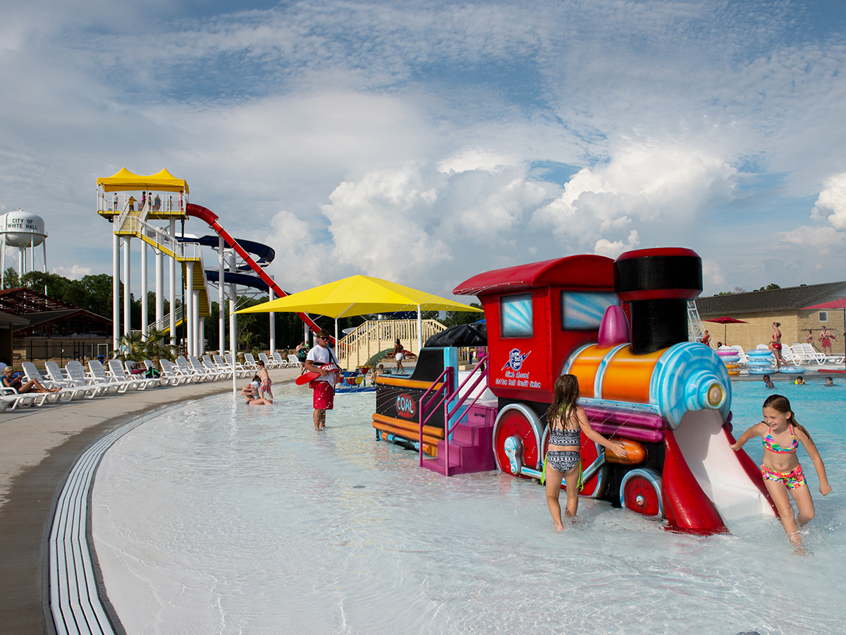 Visitors at Crenshaw Springs Water Park play in water near train feature